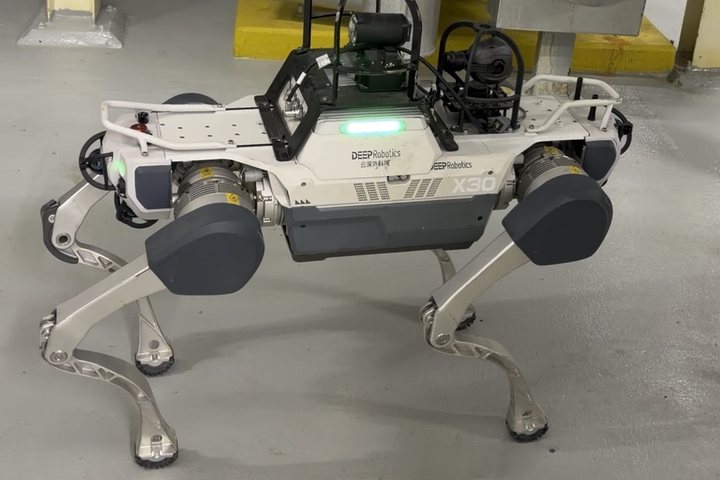 Quadruped inspection robot walking between insulated pipes and valves in a plant room